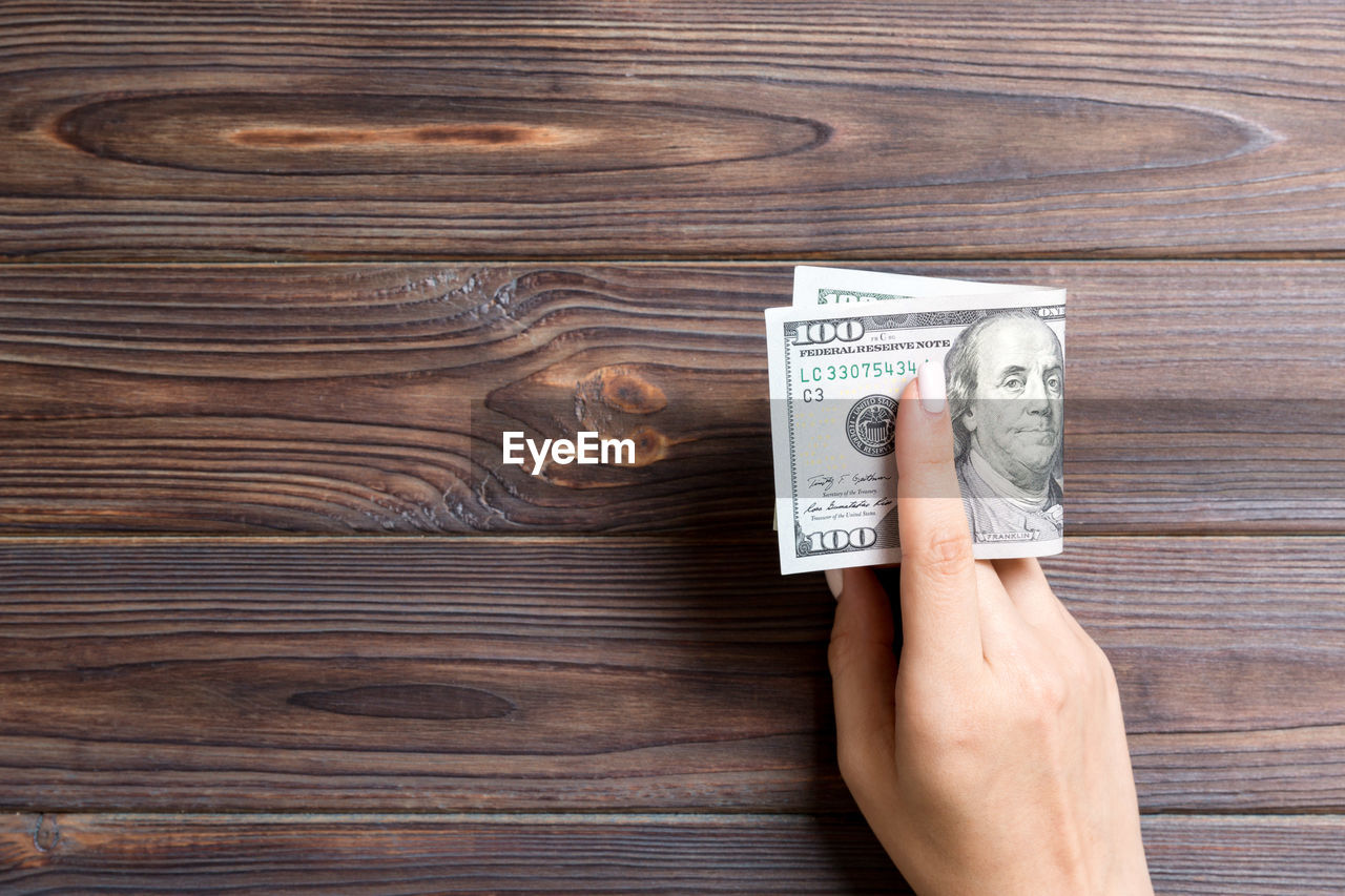 Directly above shot of woman hand holding paper currency on wooden table