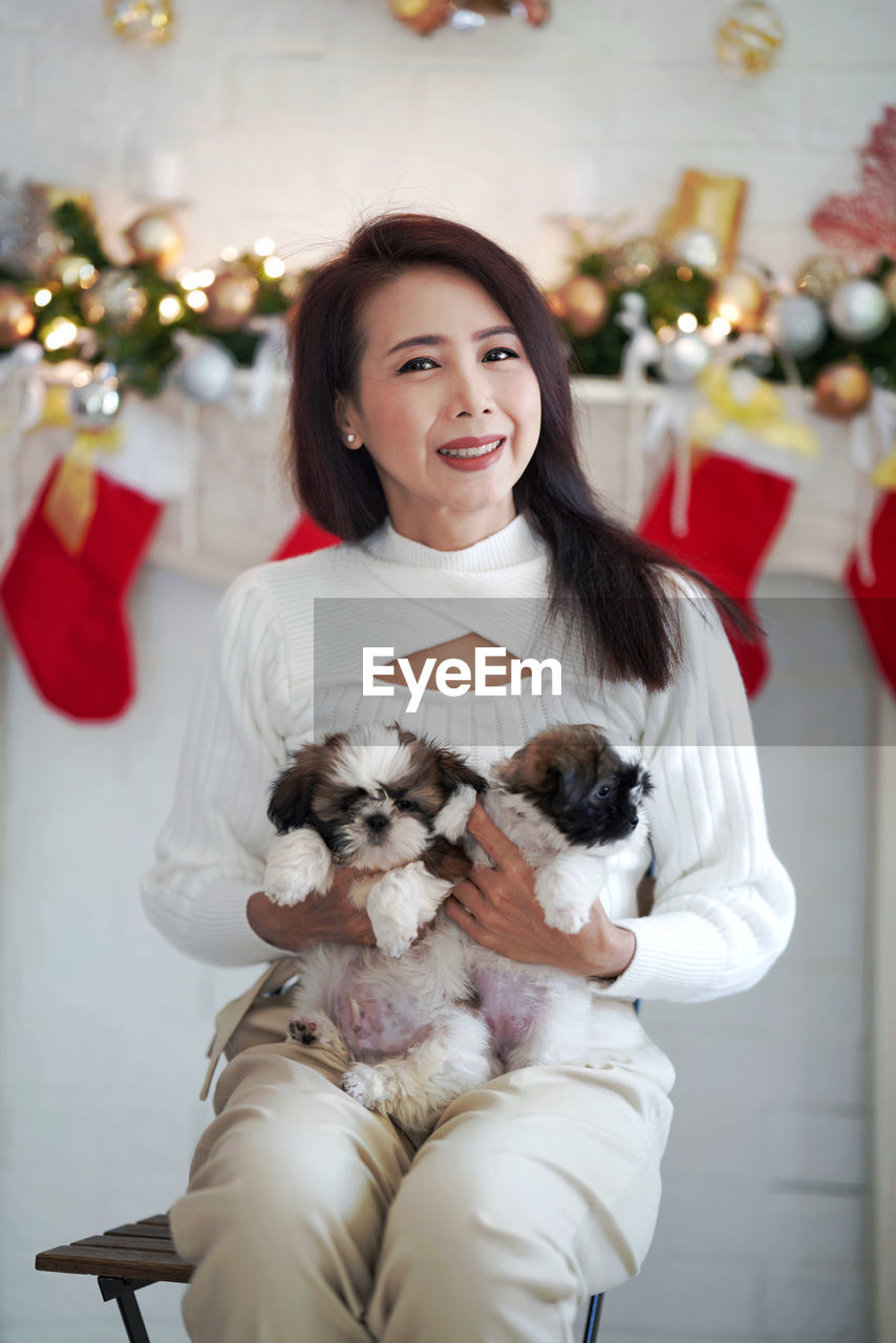 Beautiful woman in white dress hold two shih tzu puppies at home.