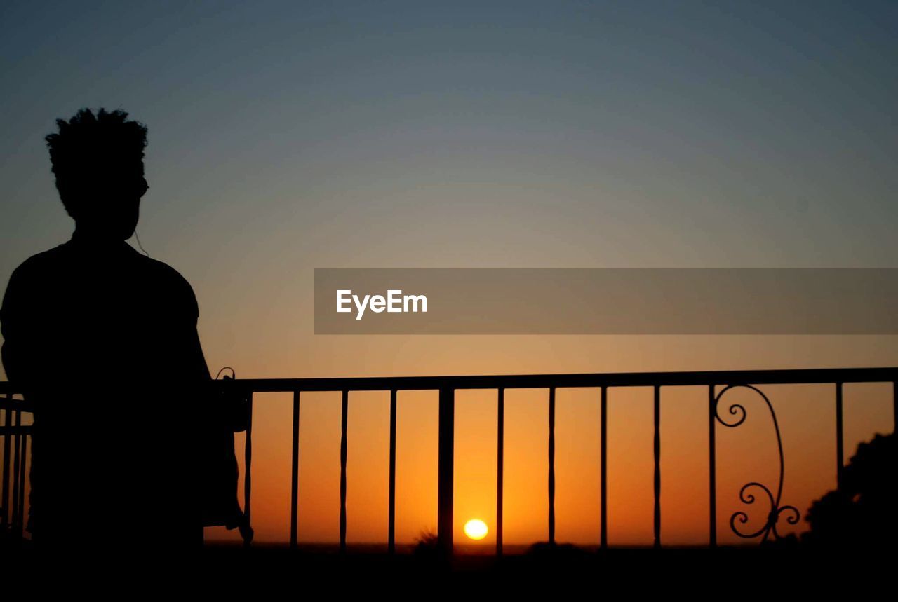 REAR VIEW OF SILHOUETTE MAN STANDING AGAINST CLEAR SKY AT SUNSET