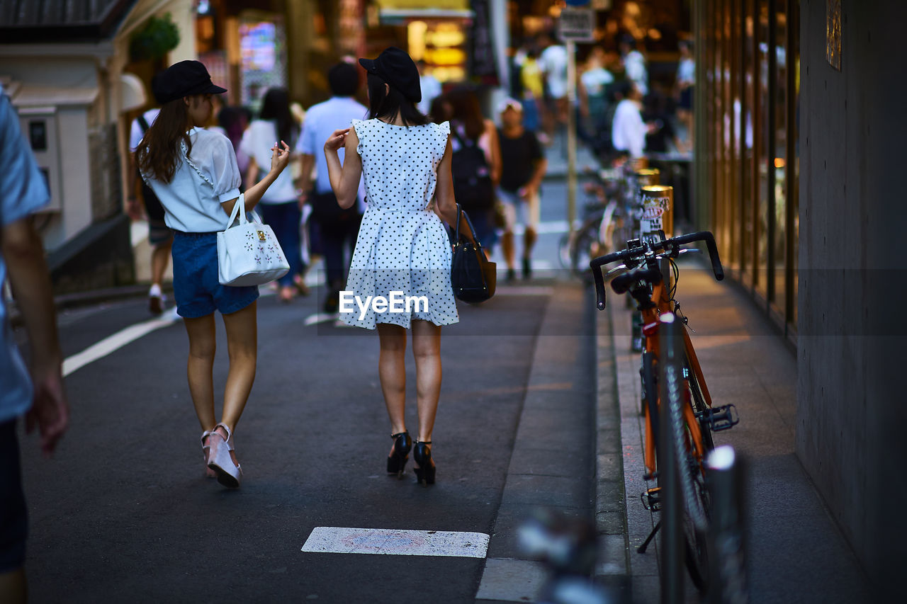 Rear view of people walking on street by bicycles in city