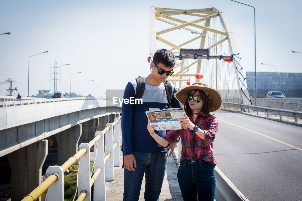 Couple reading map while standing on bridge in city