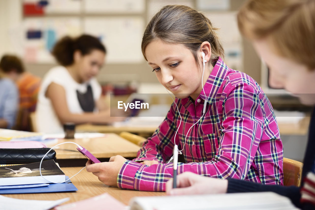 Schoolgirl listening music through smart phone in classroom