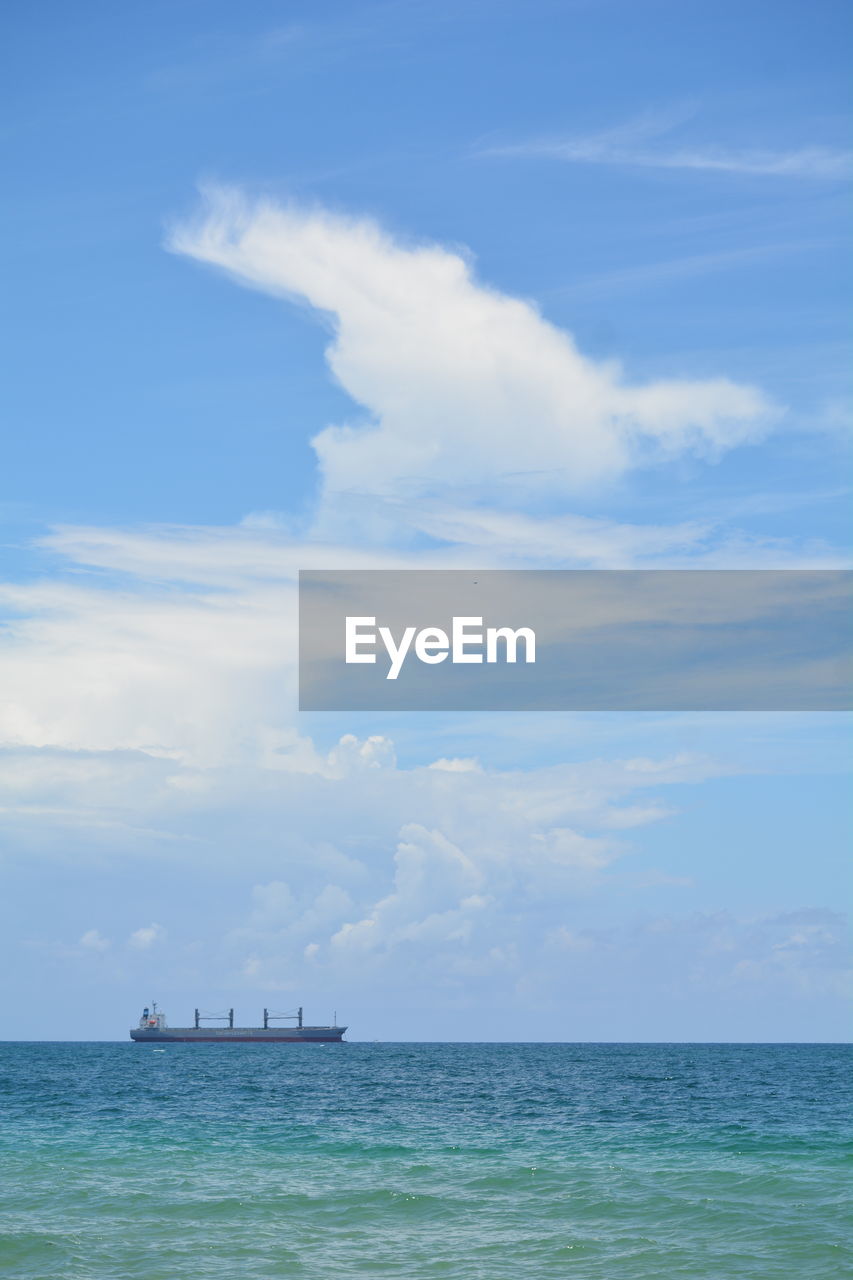 Scenic view of sea against sky with freight ship and cloud