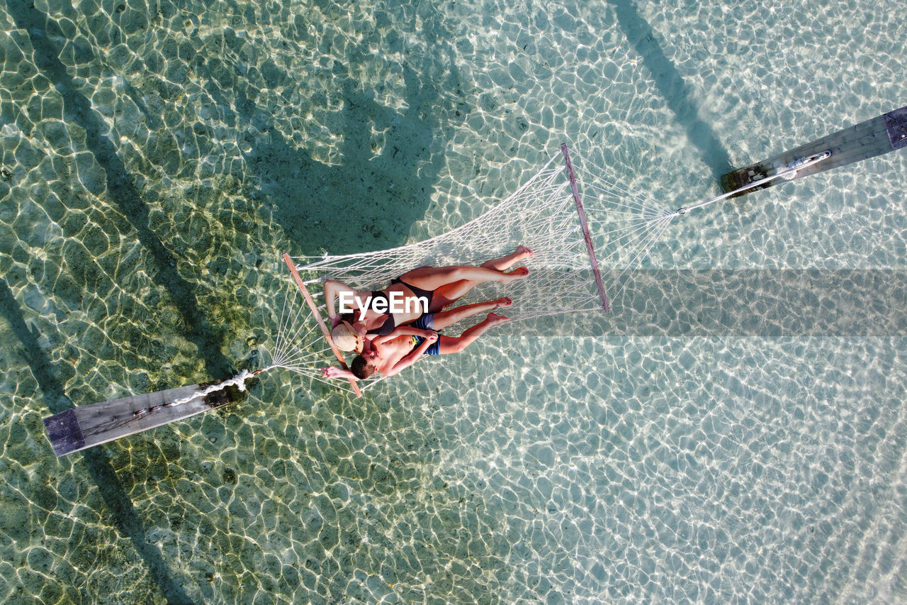 Mother and son relaxing on a hammock over the water. air view.