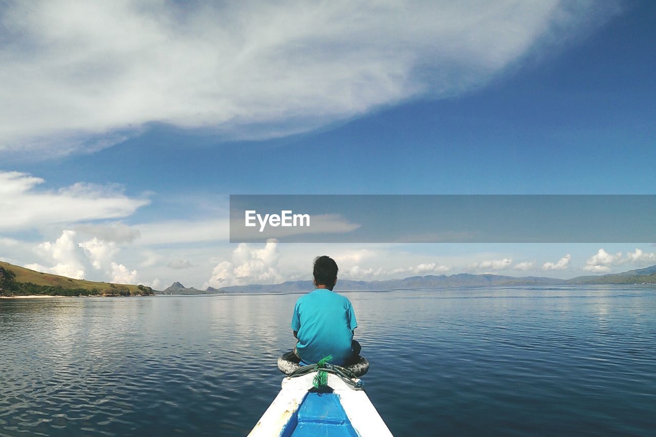 Rear view of man sitting on boat in lake against sky