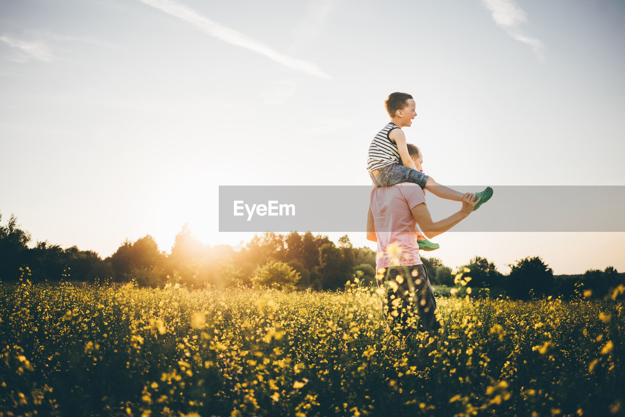 side view of young woman standing on field against sky during sunset