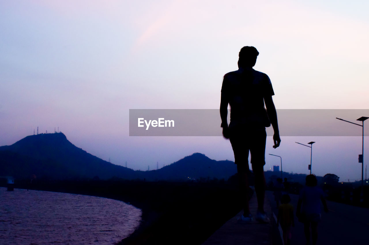 Rear view of silhouette man walking on mountain against sky