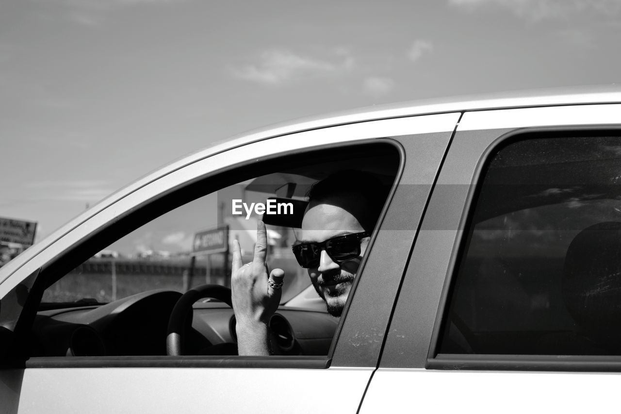 Portrait of mid adult man gesturing horn sign while driving car during sunny day