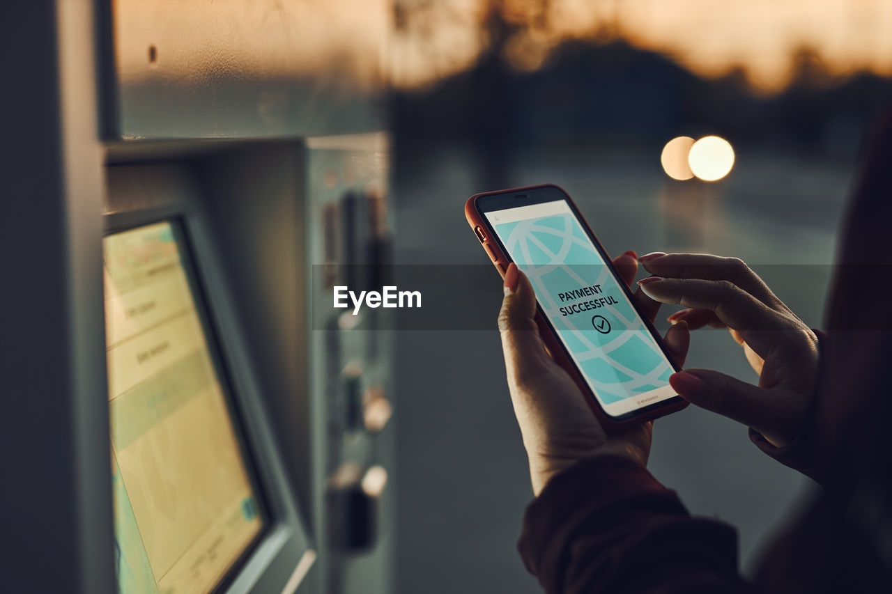 Woman buying ticket at ticket machine paying using mobile payment app on phone. public transport