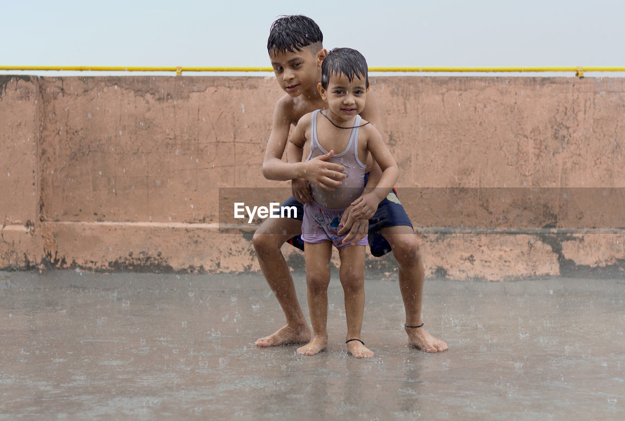 Two kids playing and having fun in rain at their terrace, outdoors during monsoon season.