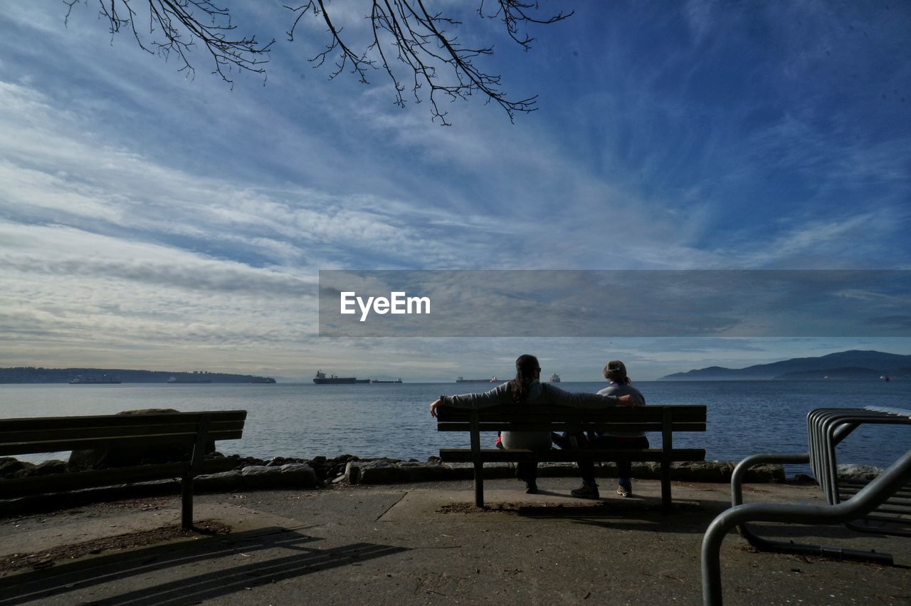 Rear view of people sitting by sea on bench