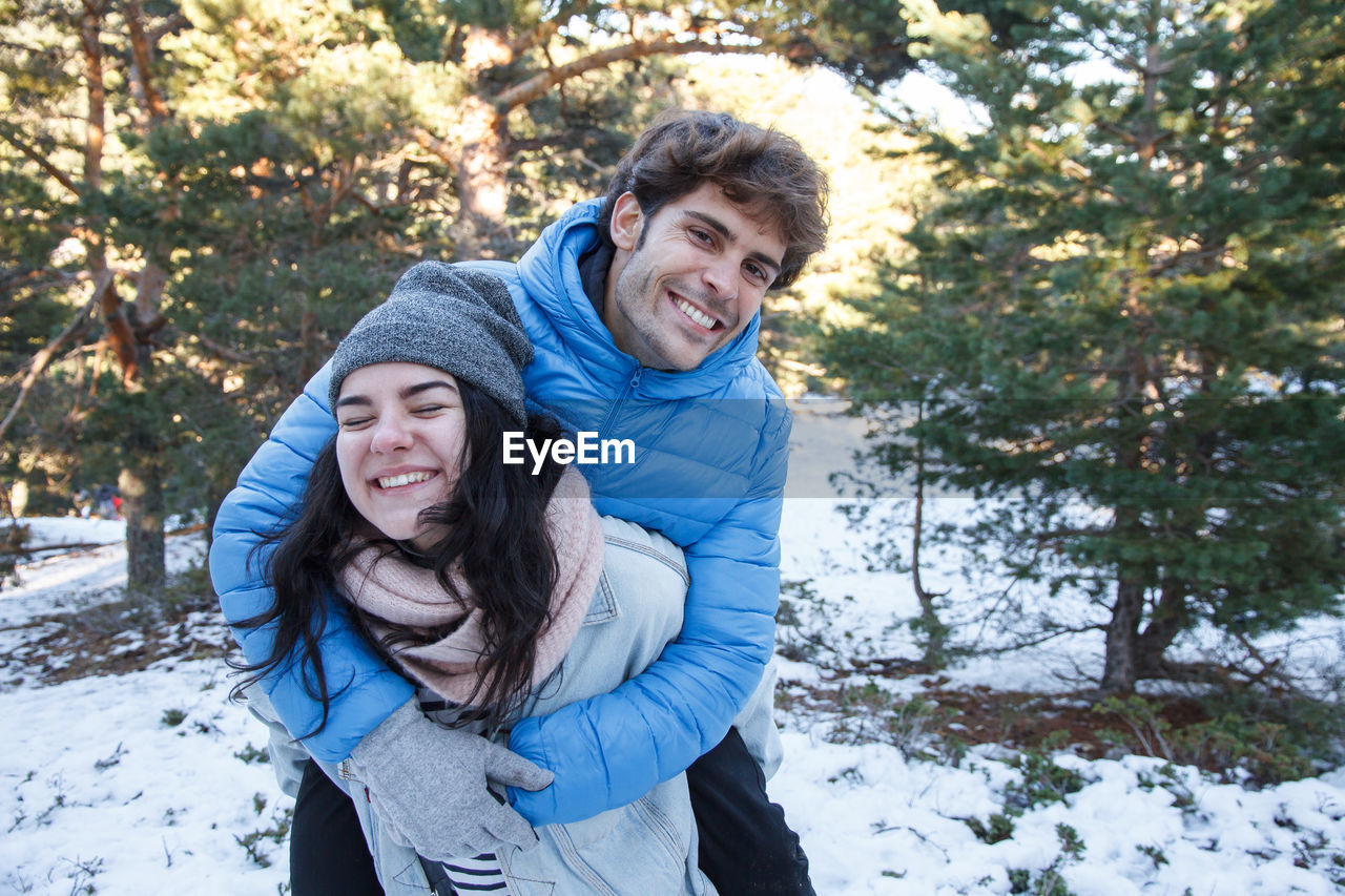 Smiling young woman giving piggyback to boyfriend on field during winter