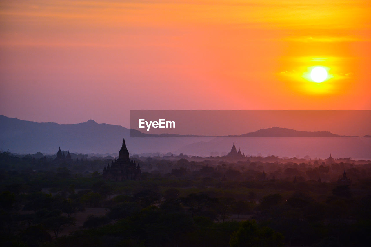 Silhouette temples on field against sky during sunset