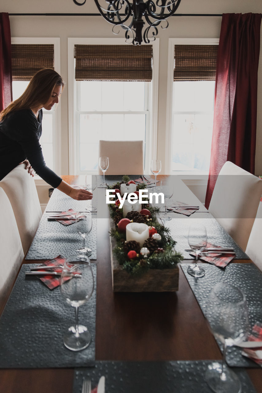 Woman placing a glass on a dining table set for a holiday dinner.