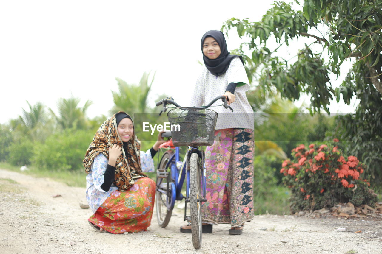 Portrait of smiling friends with bicycle on land