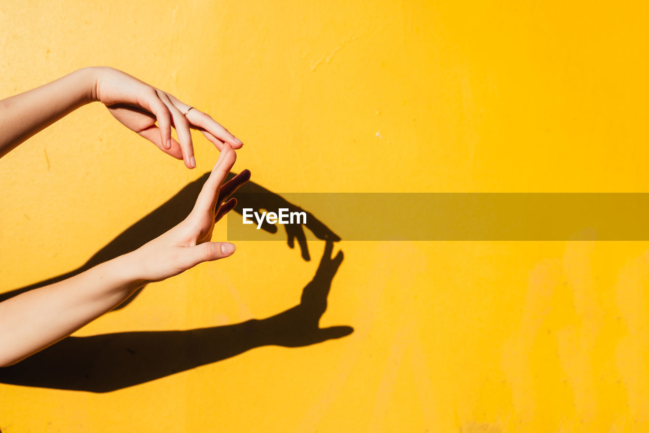 Cropped hands of woman gesturing against yellow wall