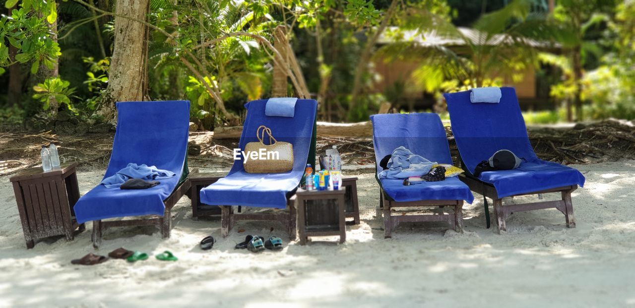 EMPTY CHAIRS ON BEACH AGAINST TREES AND BLUE SKY
