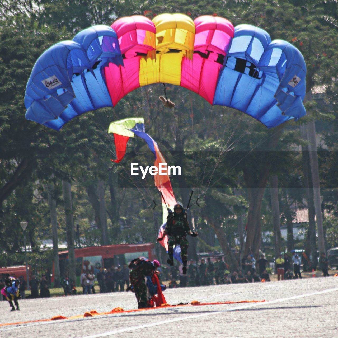 sports, extreme sports, windsports, leisure activity, nature, parachute, mid-air, adventure, flying, paragliding, day, tree, group of people, lifestyles, full length, motion, sports equipment, plant, men, parachuting, transportation, outdoors, multi colored, joy, exhilaration, fun, sky, sign, adult, recreation