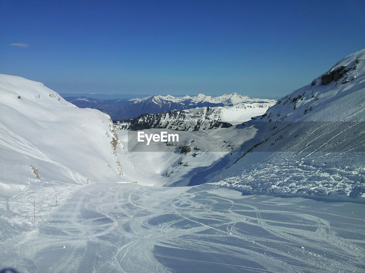 High angle view of ski tracks on snowcapped mountains against clear blue sky