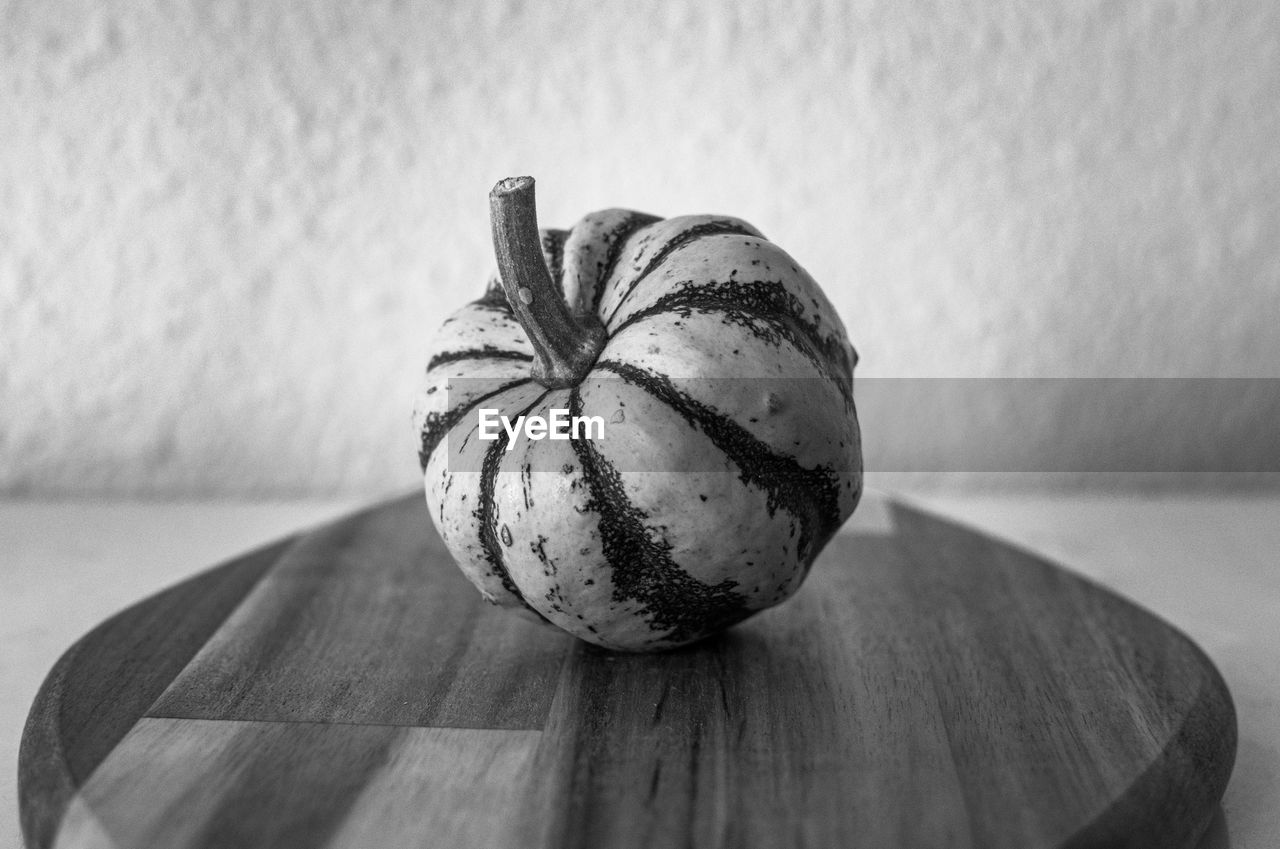 A single mini green and white decorative pumpkin displayed on a wooden chopping board monochrome