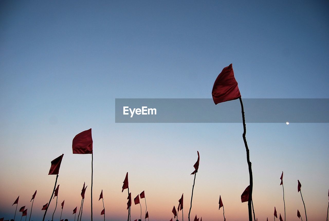 Low angle view of red flags waving against clear sky at dusk