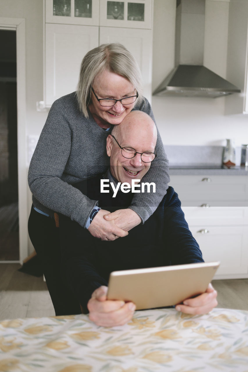 Smiling couple embracing and having video chat on tablet at kitchen table