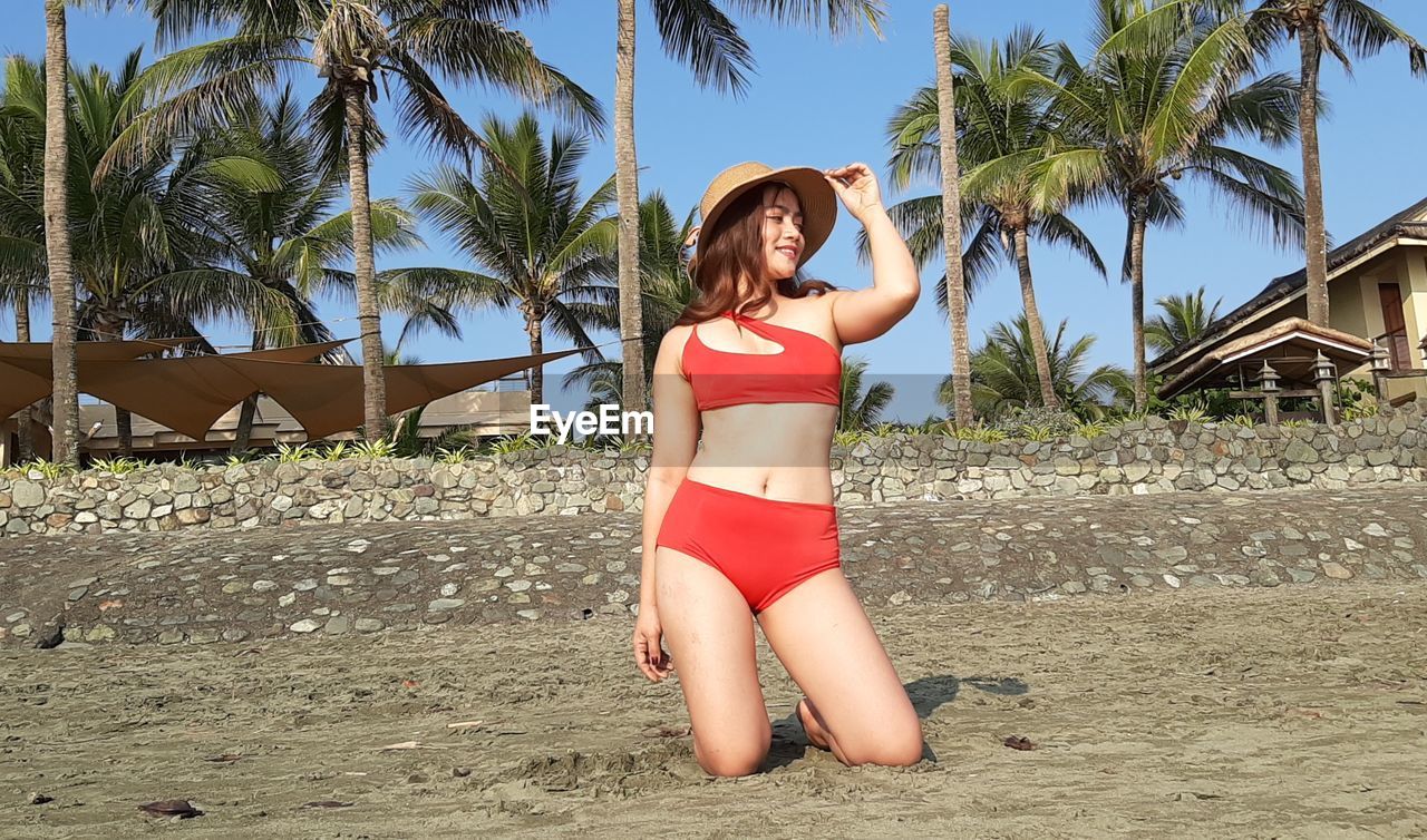 Woman in swimsuits with summer hat gainst palm trees