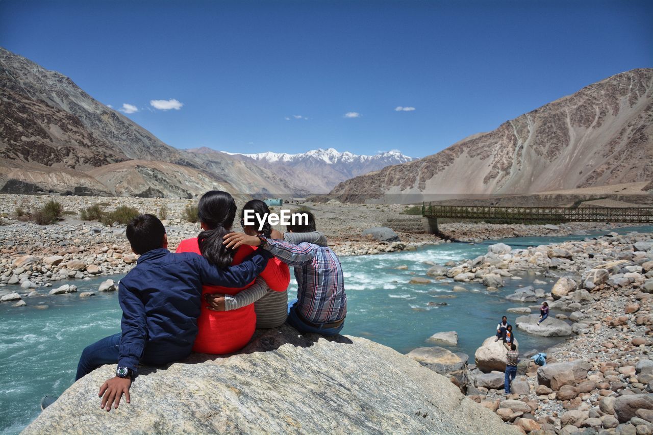 PEOPLE SITTING ON ROCKS AGAINST MOUNTAINS