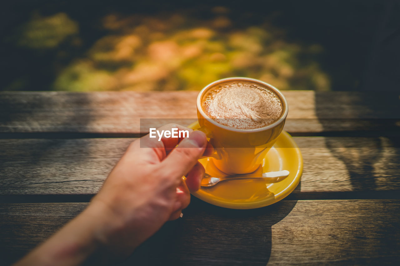 cropped hand of woman holding coffee on table