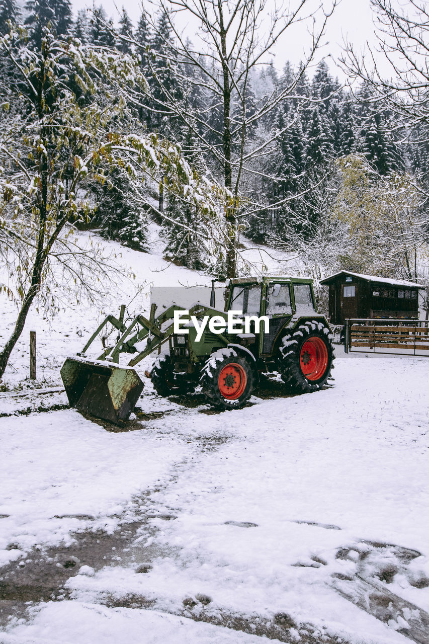 Tractor on snow covered field by trees