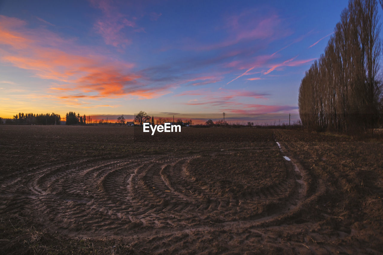 Tire tracks on farm against sky at sunset