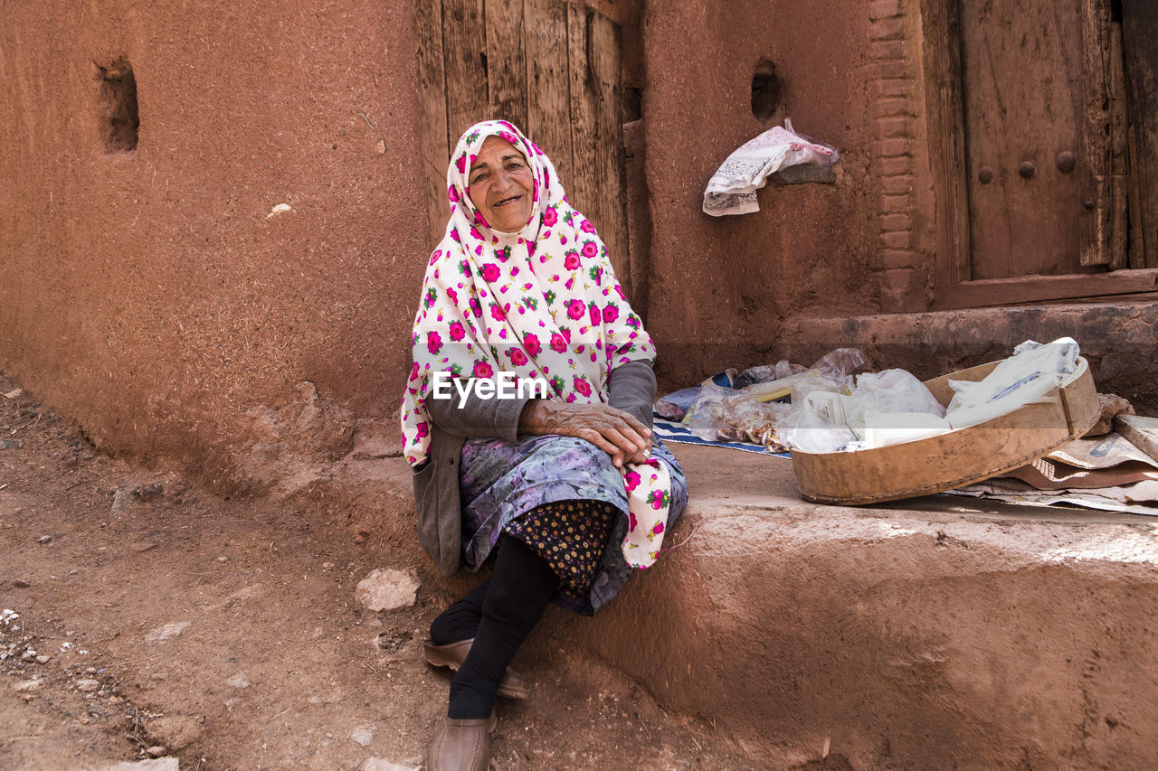 Portrait of senior woman wearing hijab sitting outside house
