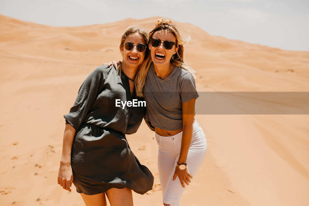 Cheerful friends standing on sand at desert against sky