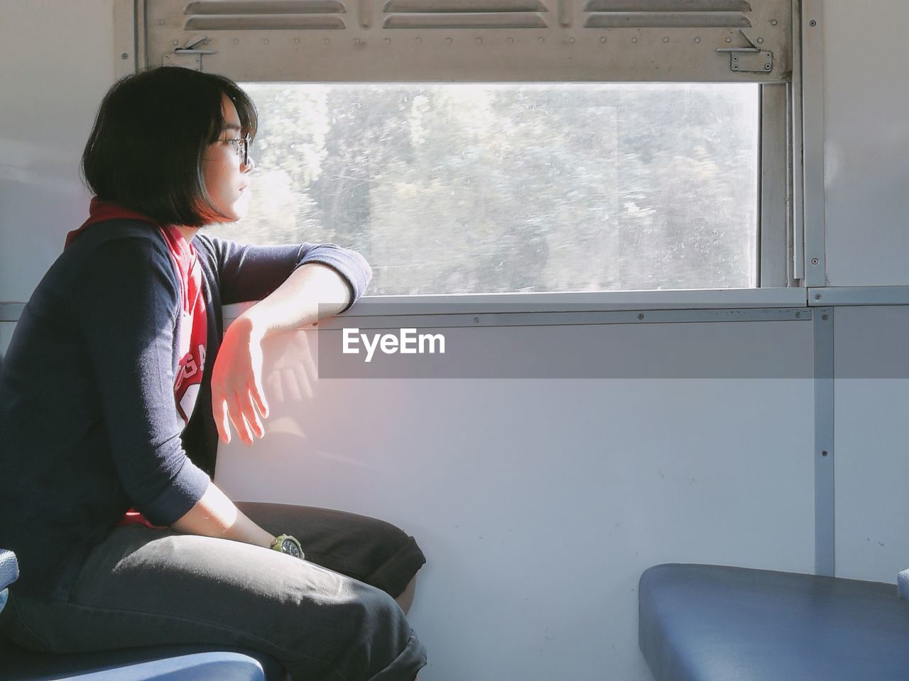 Side view of young woman sitting by window in train