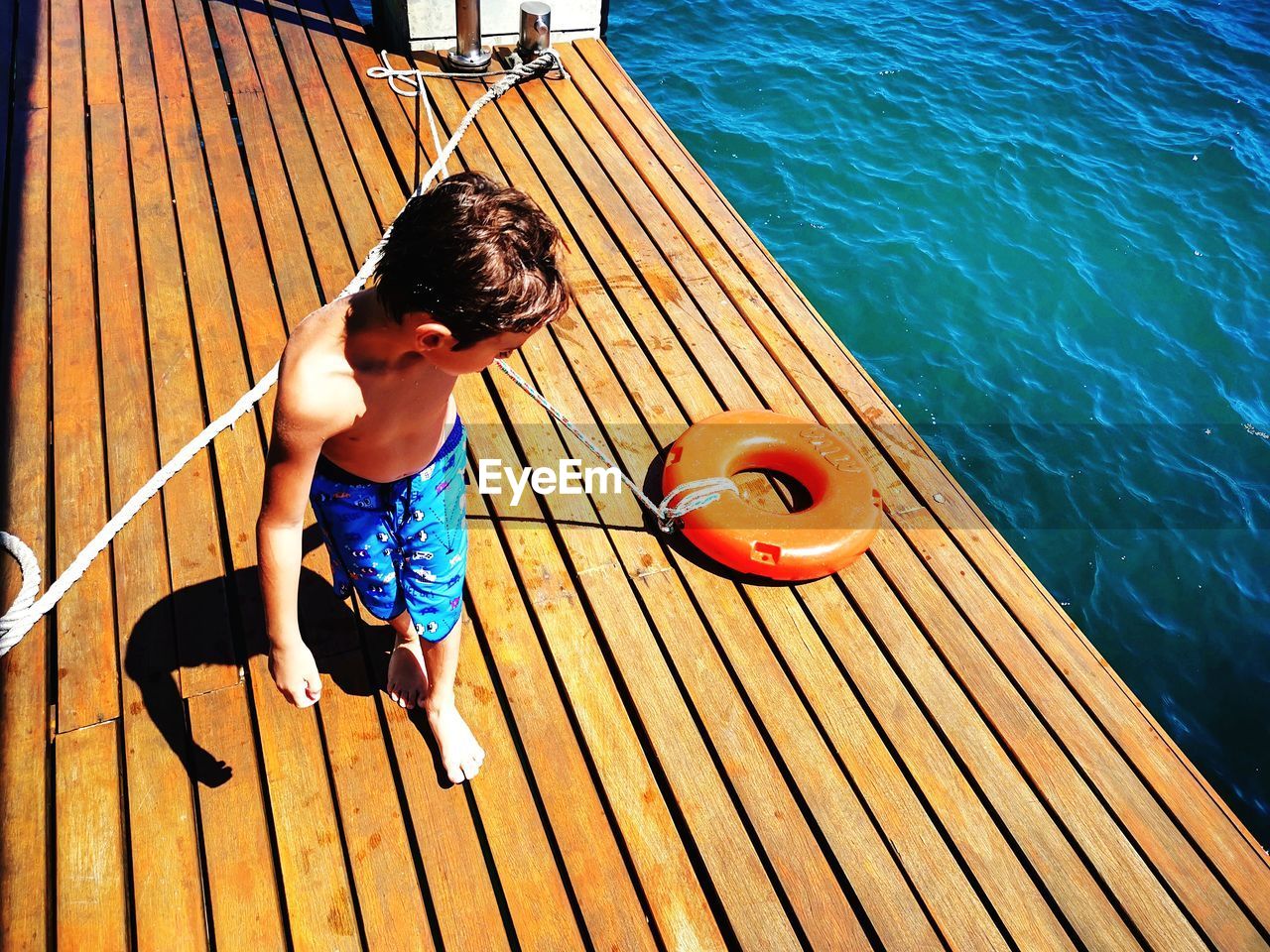 HIGH ANGLE VIEW OF BOY ON PIER OVER WATER
