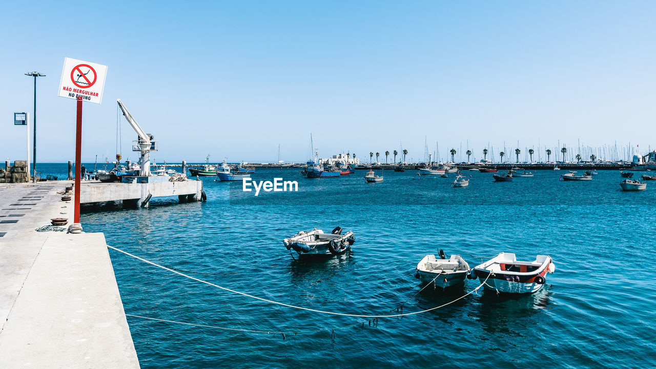 Boats in sea against clear blue sky