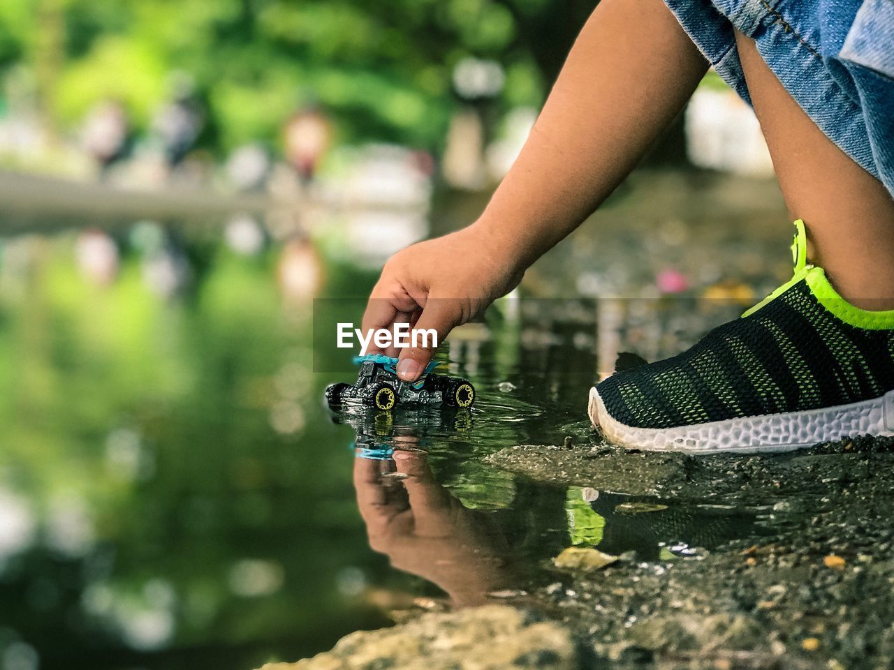 Low section of child playing with toy car in puddle