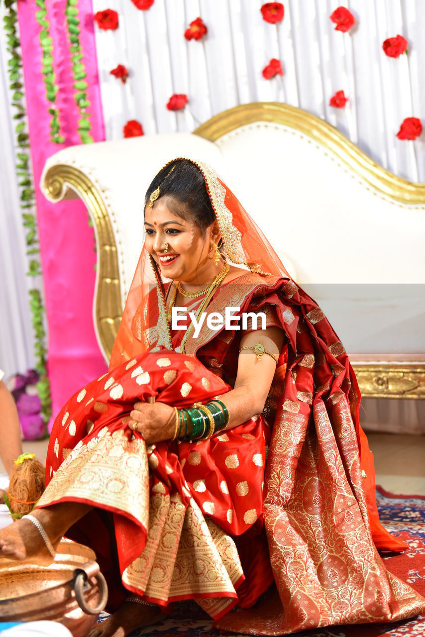 Full length of smiling bride wearing red sari looking away on stage