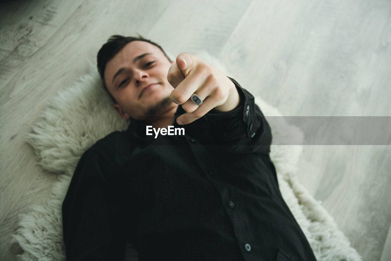 High angle portrait of man pointing while lying on rug