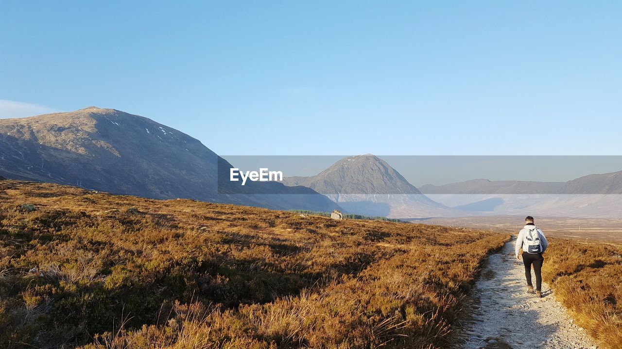 REAR VIEW OF MAN WALKING ON MOUNTAIN AGAINST SKY