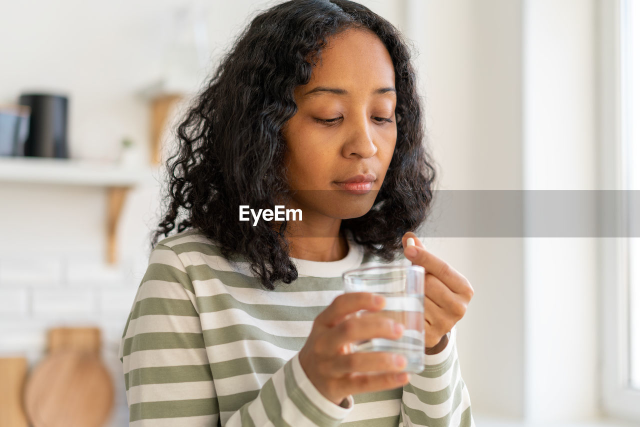 African-american female washing down pill with glass of water.healthy supplement remedy treatment