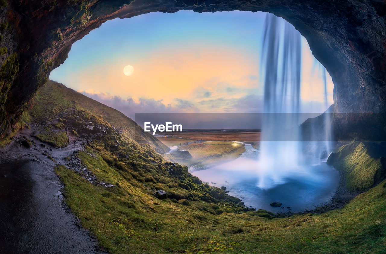 Scenic view of waterfall against sky during sunset seen through cave