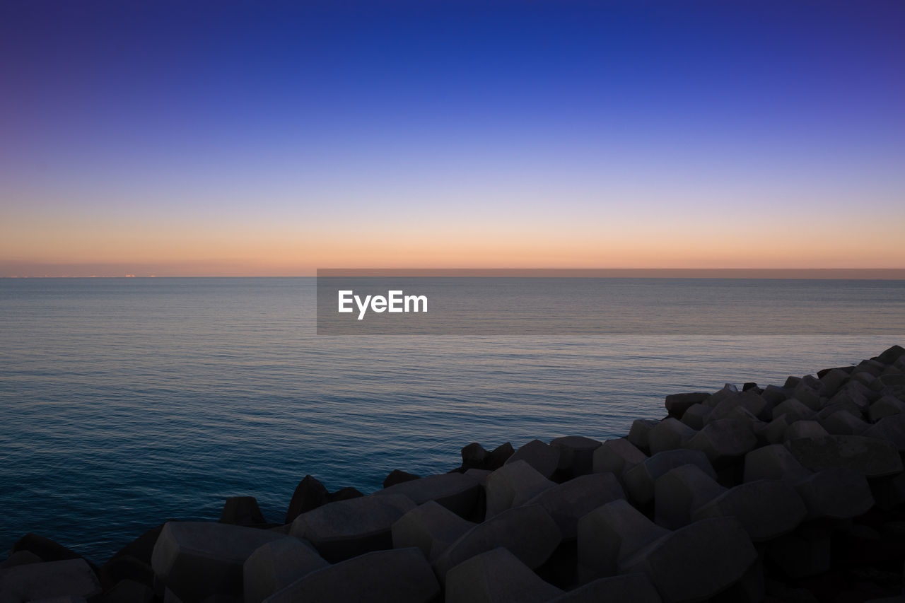 horizon, sky, sea, water, sunrise, dawn, horizon over water, ocean, scenics - nature, beauty in nature, tranquility, morning, nature, tranquil scene, blue, land, sunlight, reflection, beach, coast, seascape, clear sky, no people, urban skyline, architecture, idyllic, travel destinations, travel, shore, environment, outdoors, wave, rock, bay, twilight, copy space, landscape, relaxation