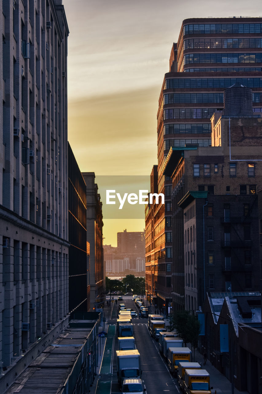 Traffic on road amidst buildings against sky during sunset