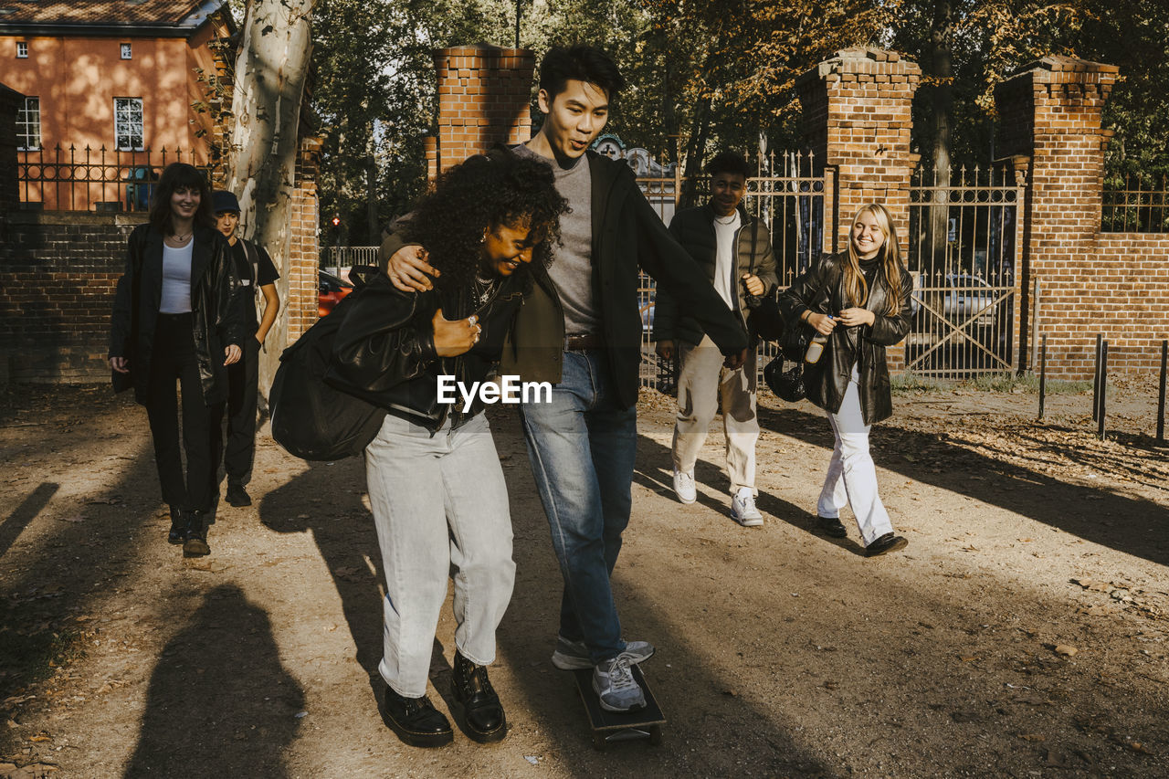 Smiling male and female friends walking in park during sunny day