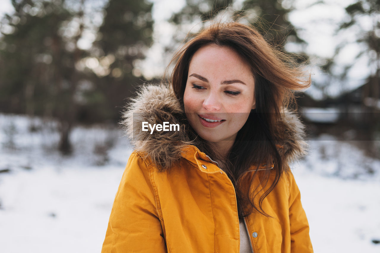 Portrait of young smiling beautiful woman in yellow jacket walking in winter forest