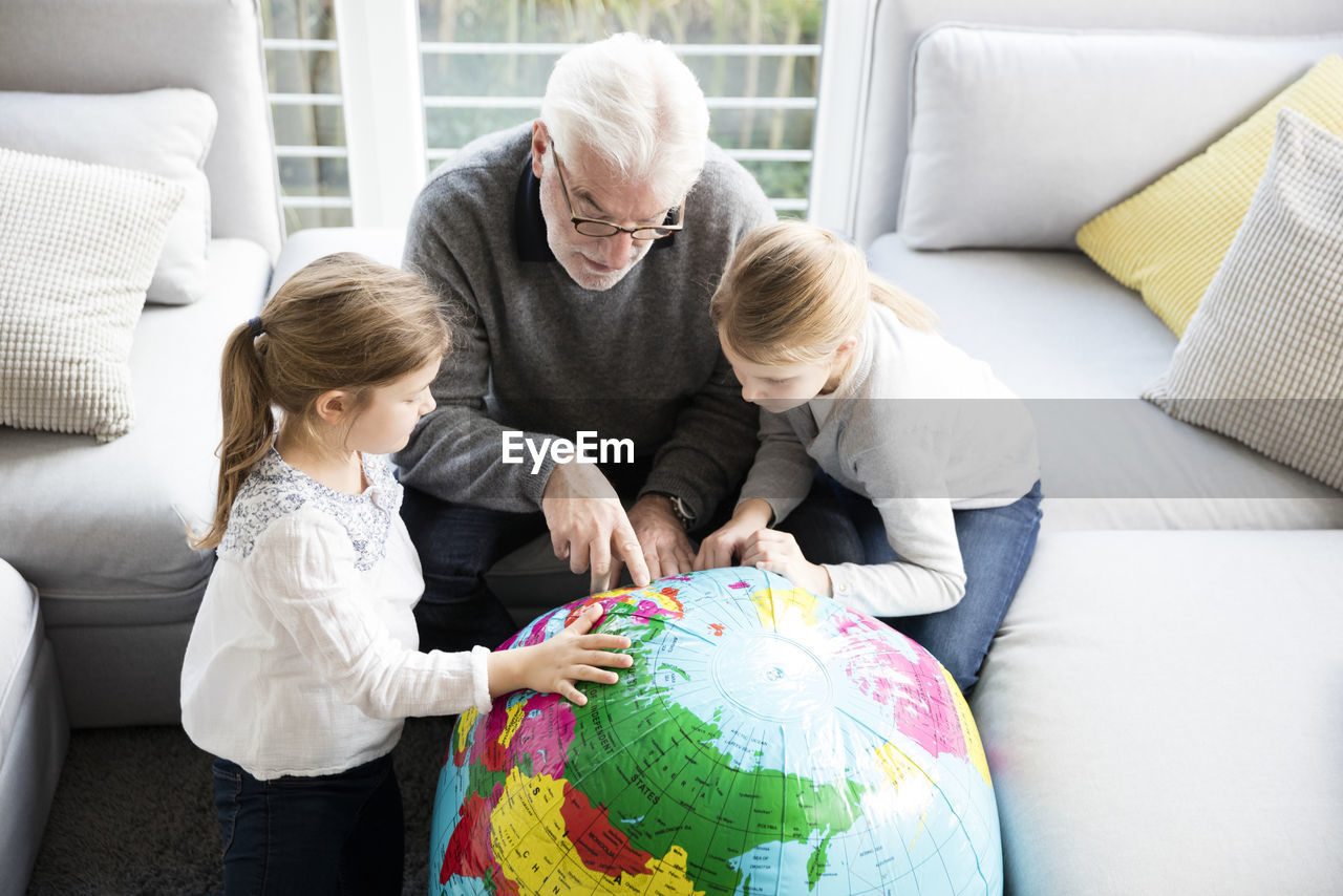 Two girls and grandfather with globe in living room