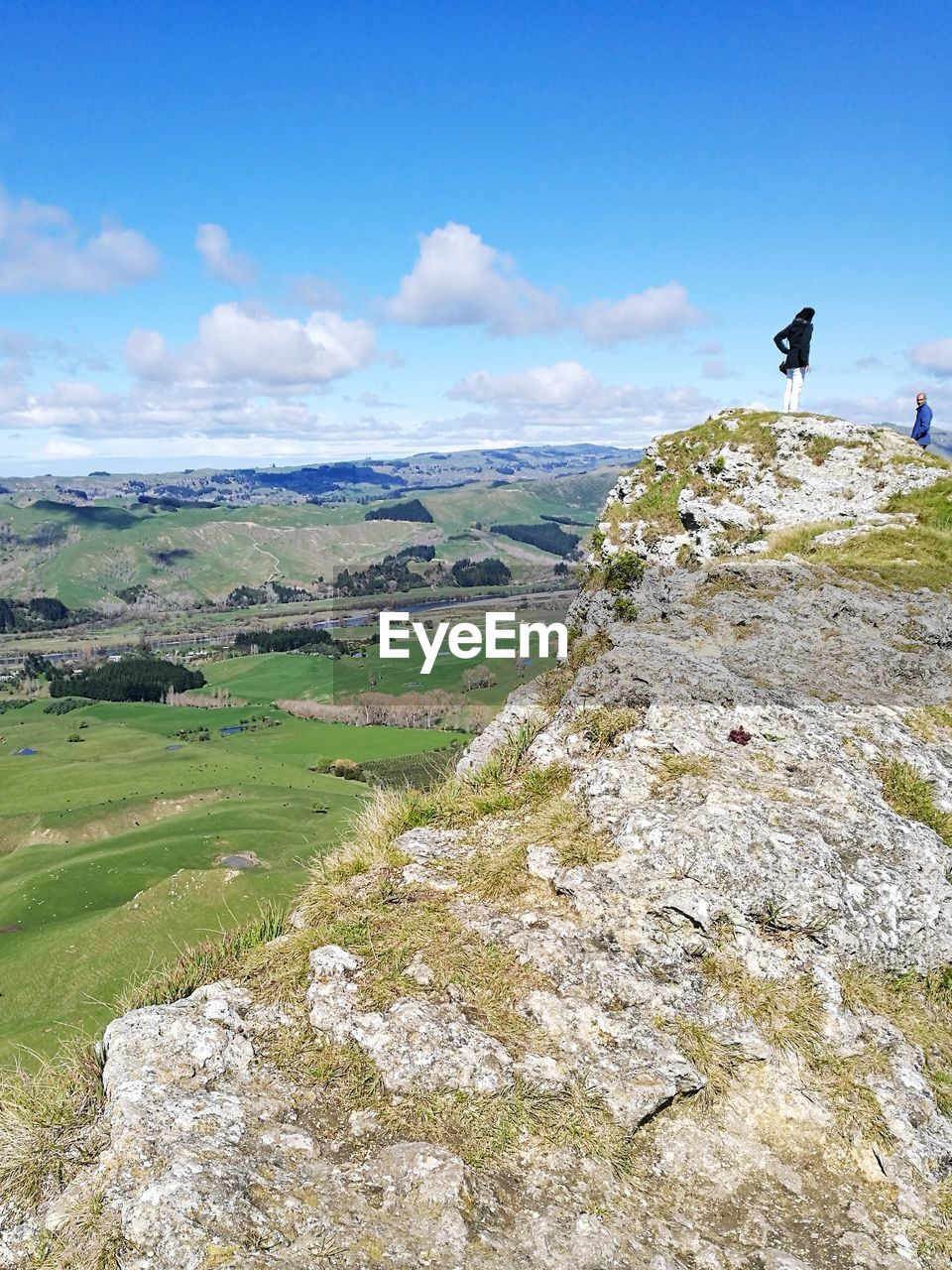 Distant view of young woman standing on cliff against sky