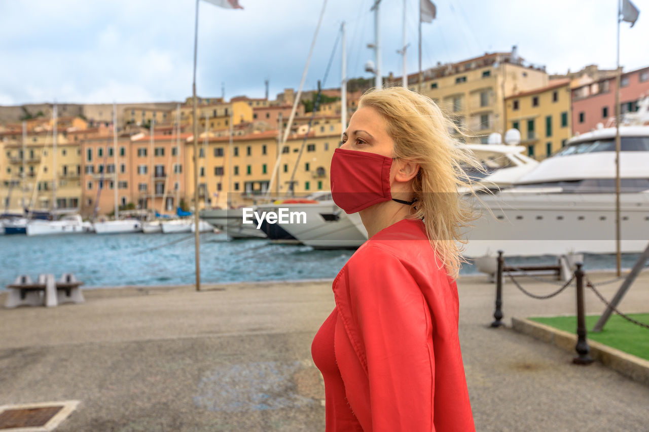 Low angle view of woman wearing mask looking away while standing against building