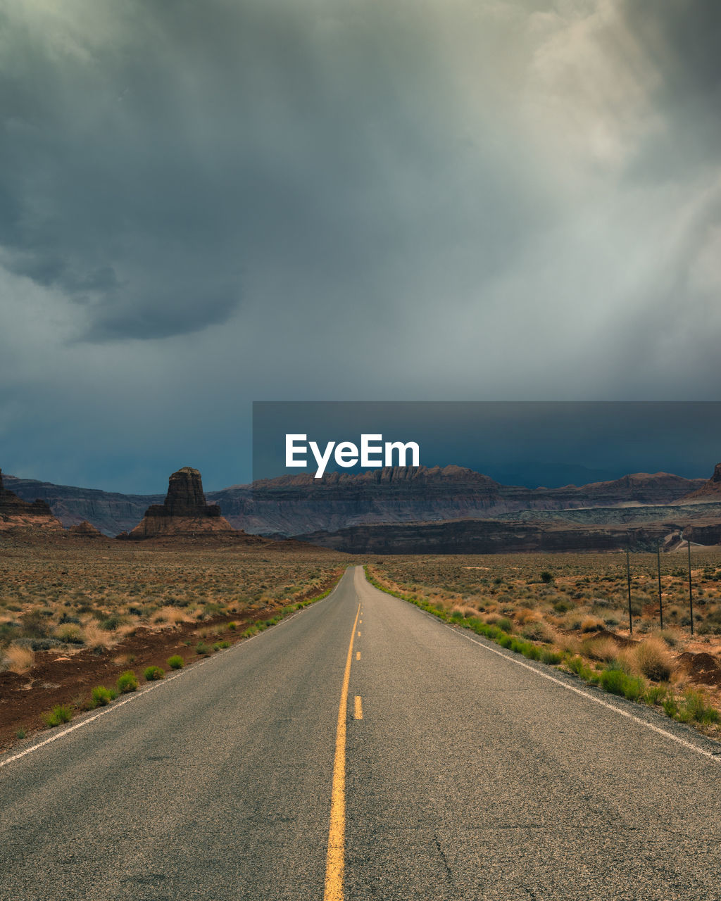 Long straight road in utah with dramatic clouds and rain rolling in, vertical image.